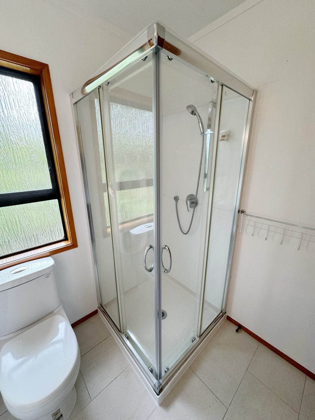 Glass shower enclosure in a bright bathroom with a window.