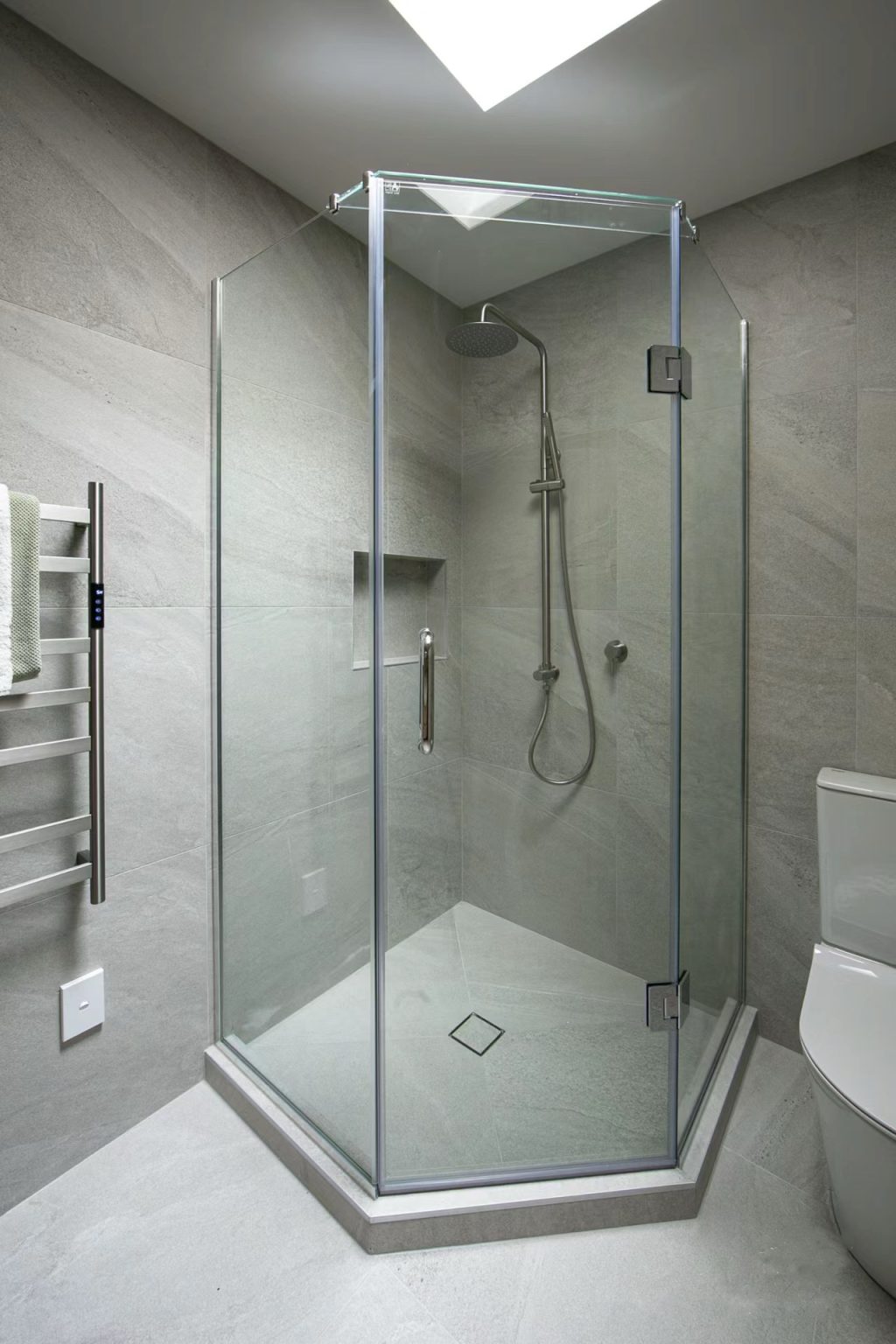 Modern glass shower with gray tile walls and overhead showerhead.