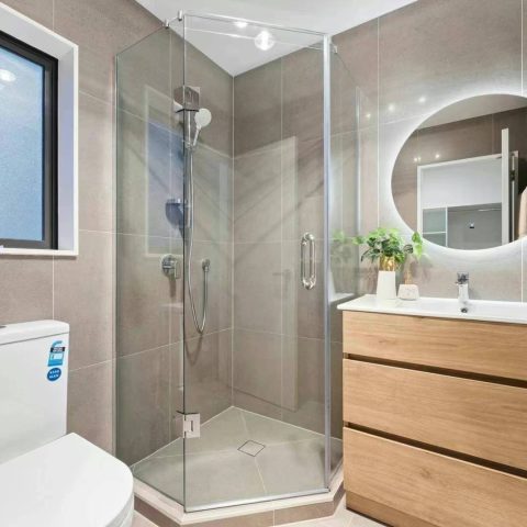 Modern bathroom with glass shower, wooden vanity, and round mirror.