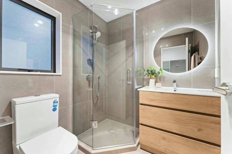 Modern bathroom with glass shower, wooden vanity, and round mirror.