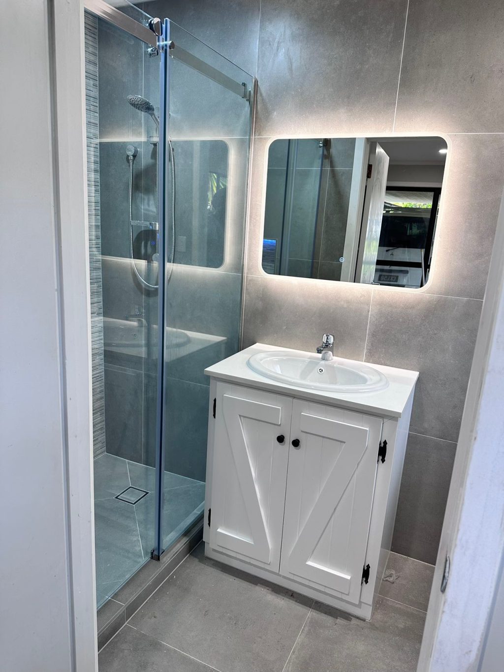 Modern bathroom with glass shower and illuminated mirror above a white vanity.