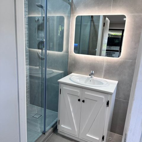 Modern bathroom with glass shower and illuminated mirror above a white vanity.