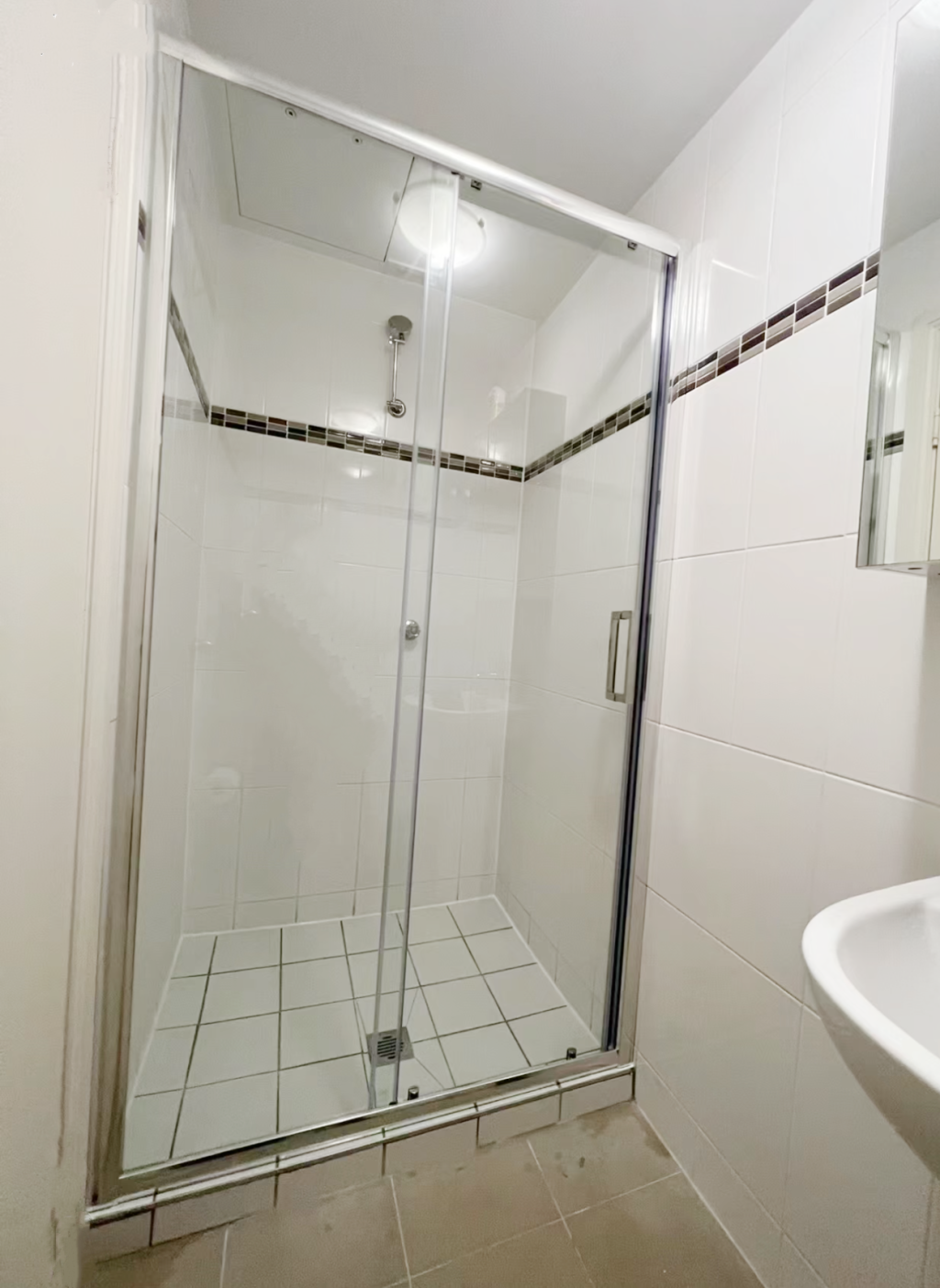 Glass shower enclosure with white tiled walls and floor.