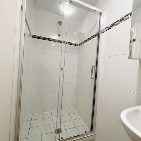 Glass shower enclosure with white tiled walls and floor.