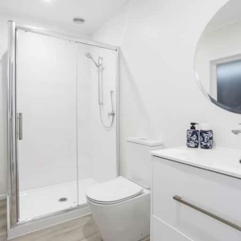 Modern bathroom with glass shower, white fixtures, and round mirror.
