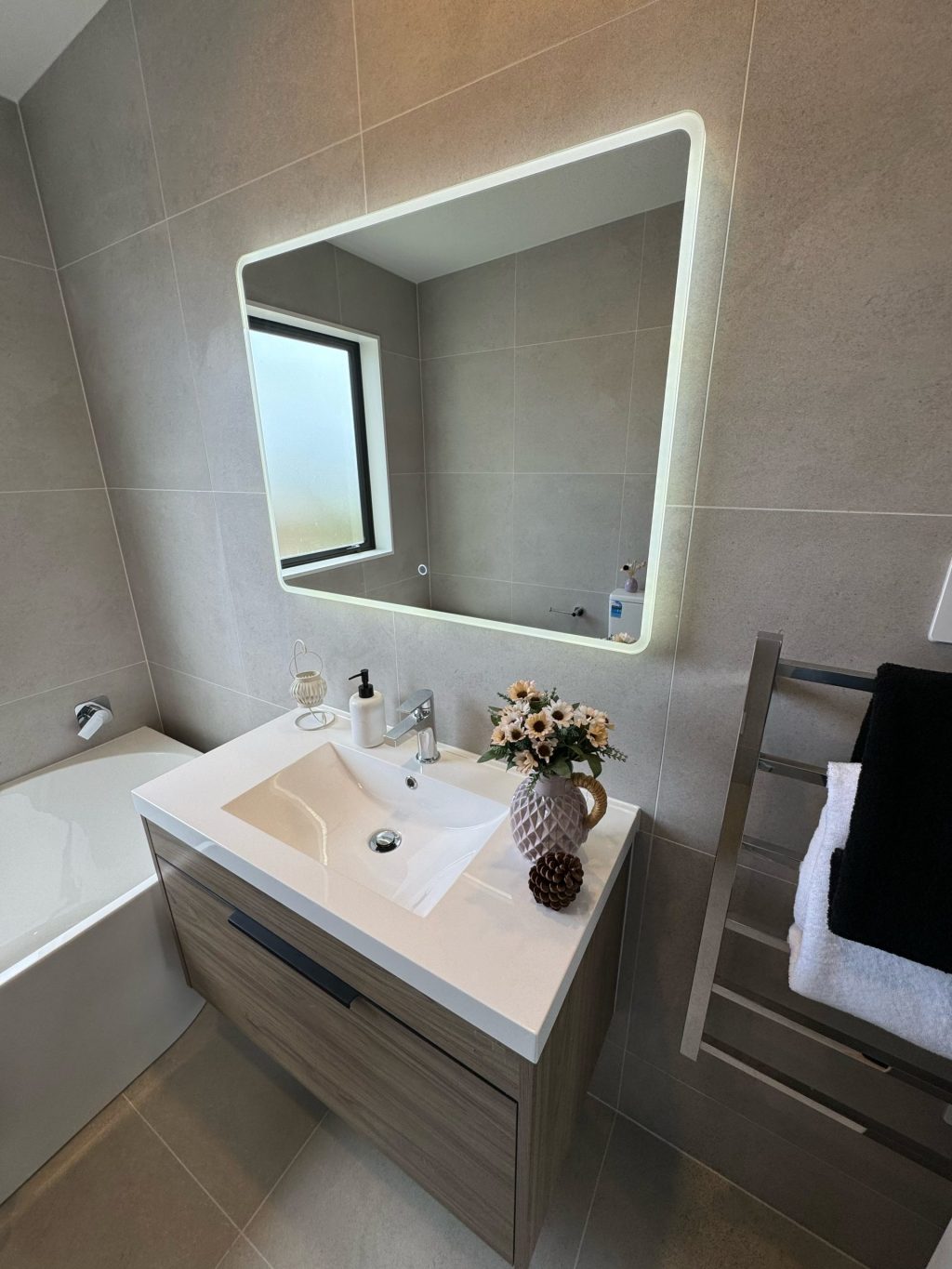 Modern bathroom with illuminated mirror, sink, and decorative flowers.