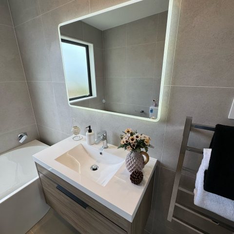 Modern bathroom with illuminated mirror, sink, and decorative flowers.
