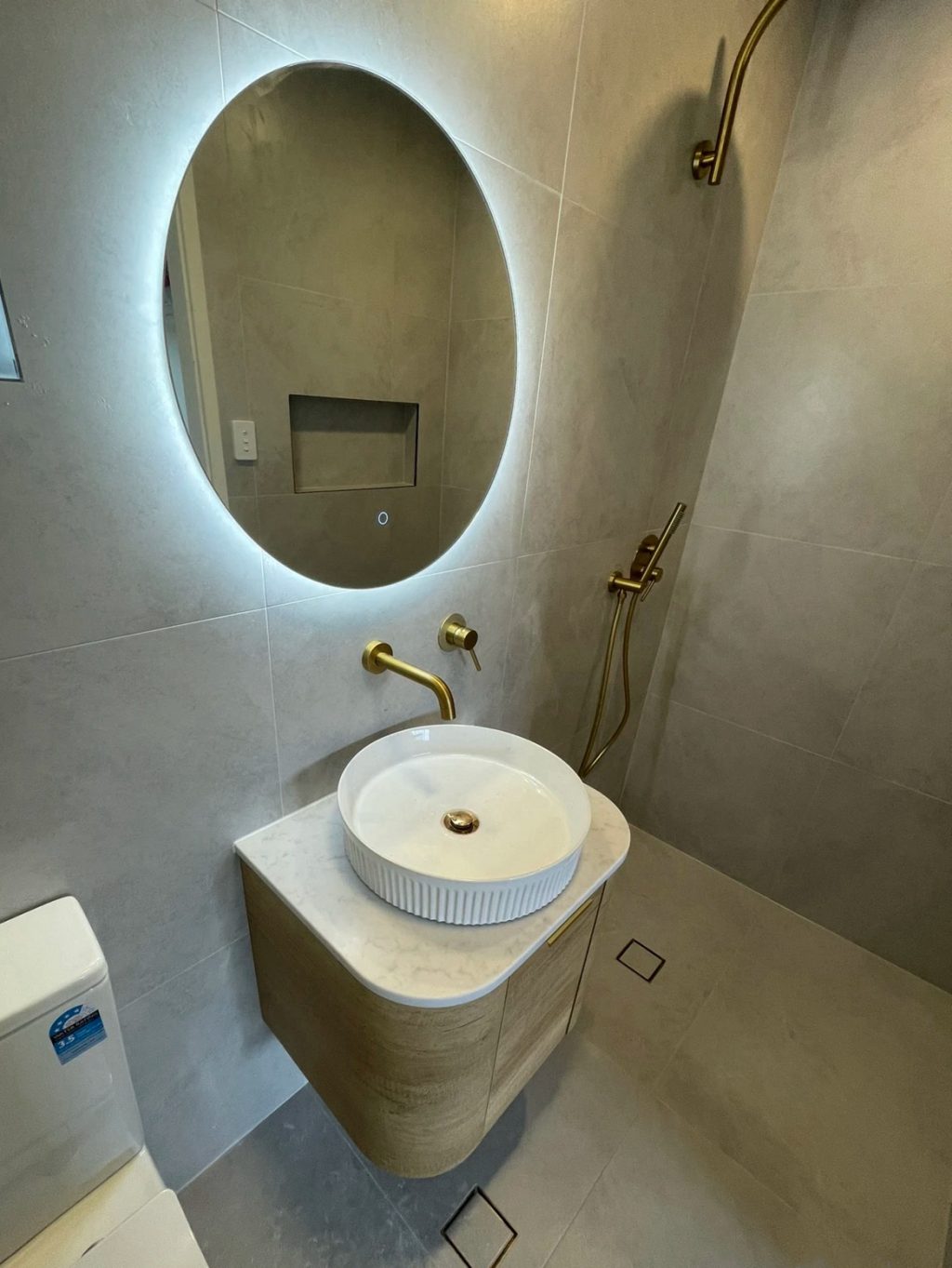 Modern bathroom with round mirror, vessel sink, and gold fixtures.