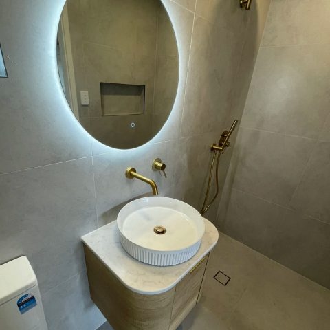 Modern bathroom with round mirror, vessel sink, and gold fixtures.