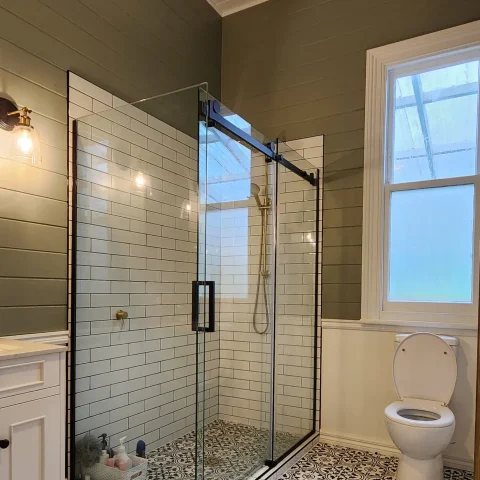 Modern bathroom with glass shower, white tiles, and toilet.
