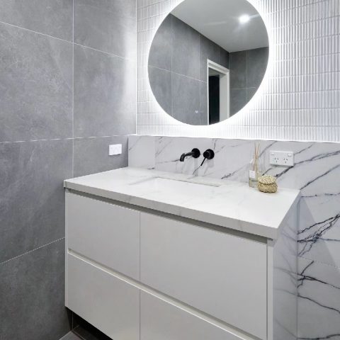Modern bathroom with marble sink, round mirror, and gray tiled walls.