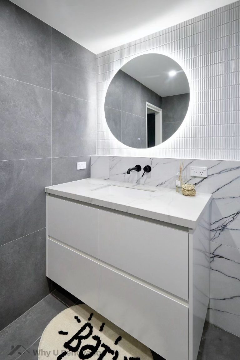 Modern bathroom with marble sink, round mirror, and gray tiled walls.