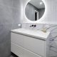 Modern bathroom with marble sink, round mirror, and gray tiled walls.