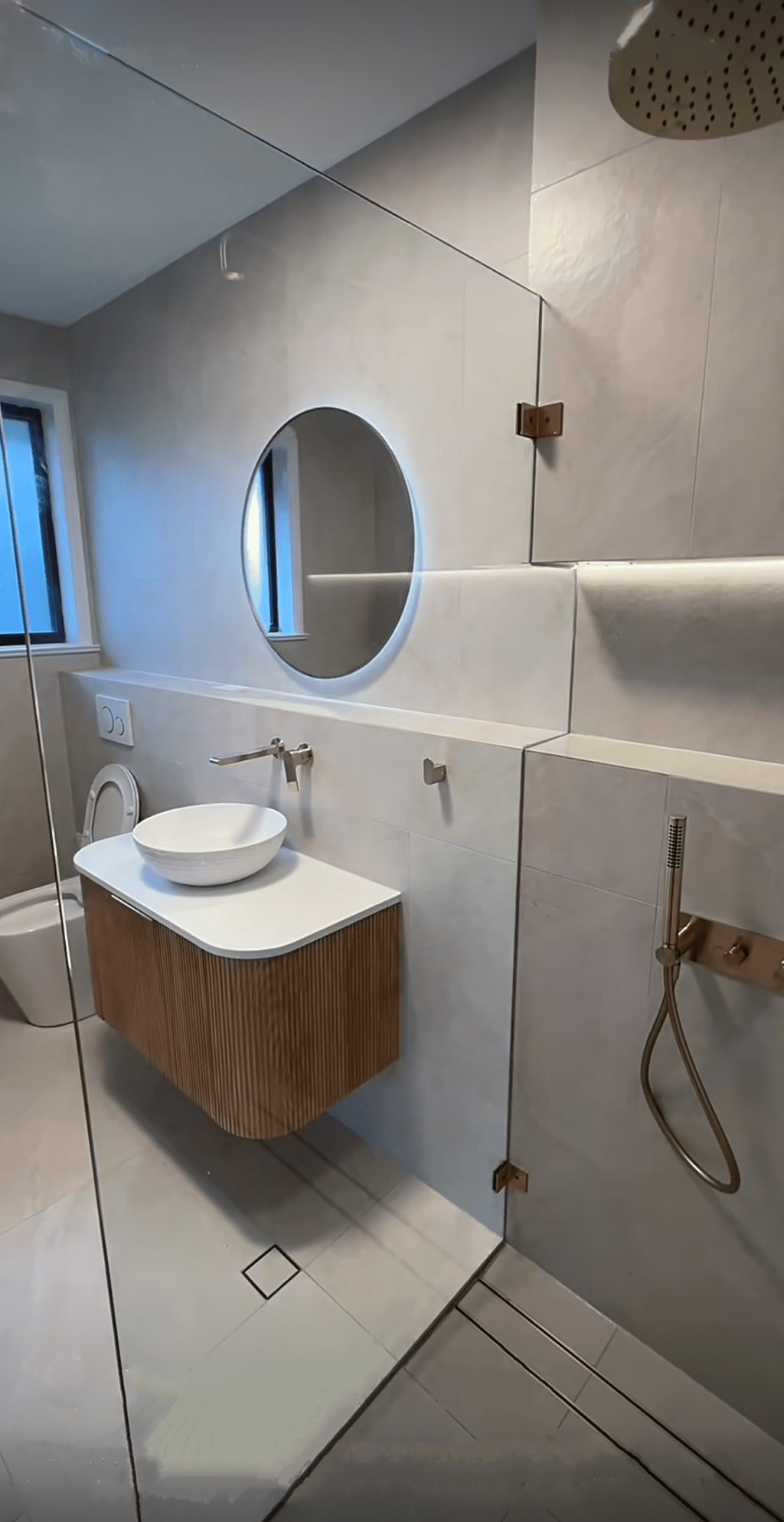 Modern bathroom with round mirror, glass shower, and freestanding bathtub.