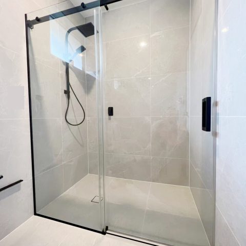 Glass shower enclosure with black fixtures in a modern bathroom.