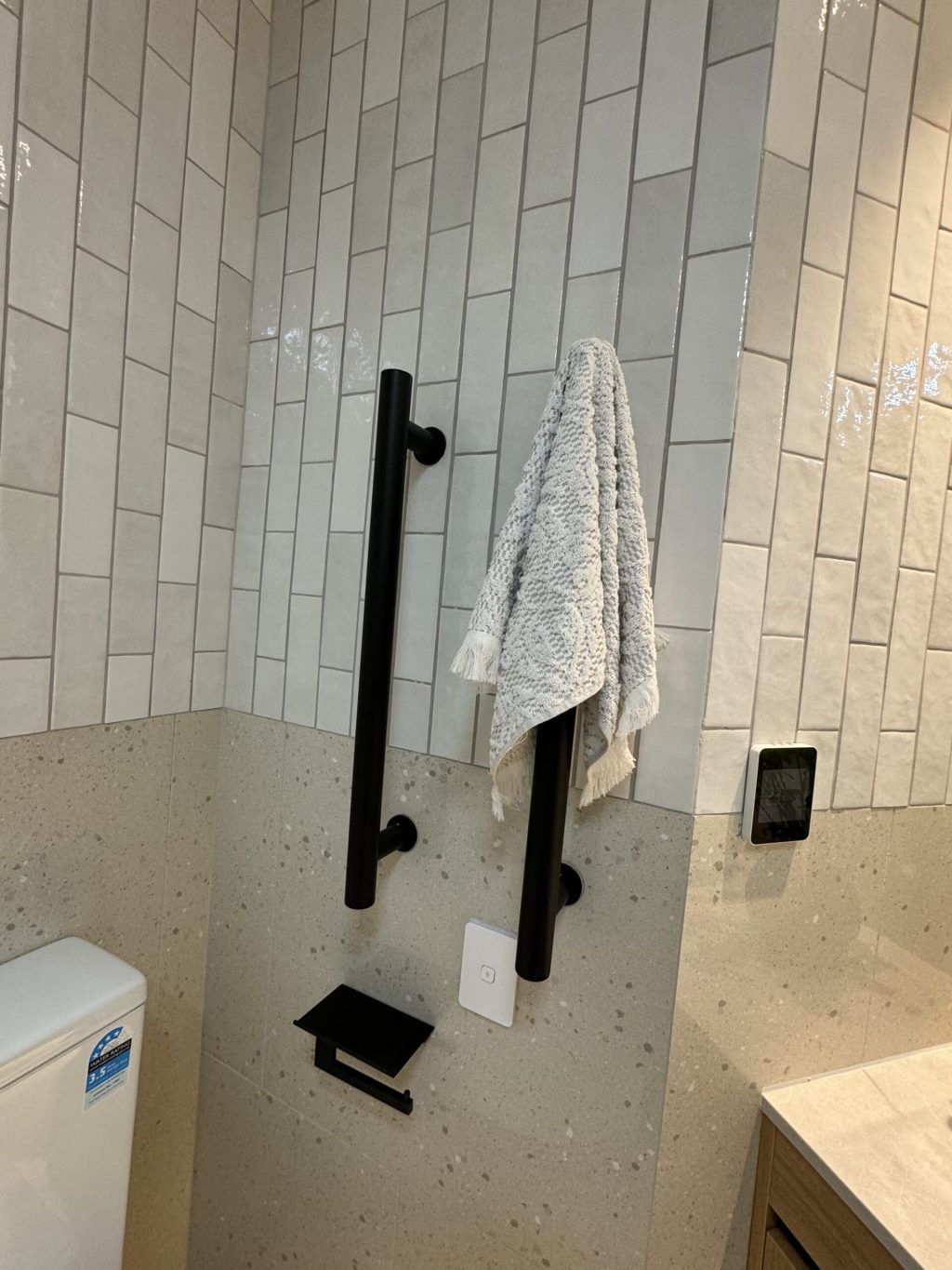 Towel hanging on black grab bar in tiled bathroom.
