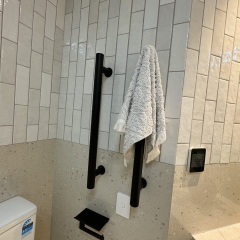 Towel hanging on black grab bar in tiled bathroom.