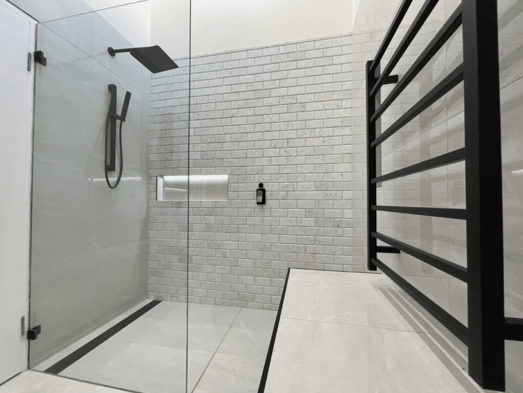 Modern shower with glass door, black fixtures, and white subway tiles.