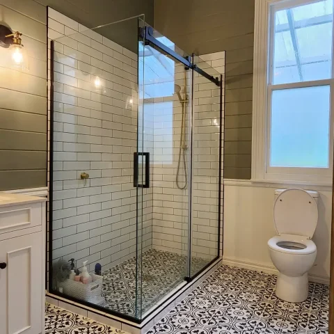 Modern bathroom with glass shower, white tiles, and patterned floor.