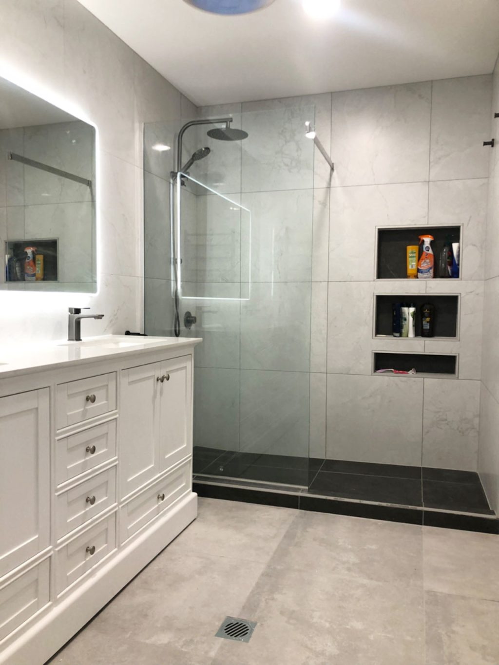 Karita1800 white-2 Modern bathroom with glass shower, white vanity, and illuminated mirror.