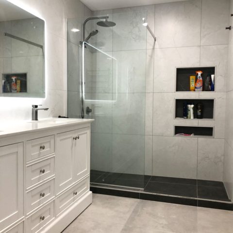 Modern bathroom with glass shower, white vanity, and illuminated mirror.