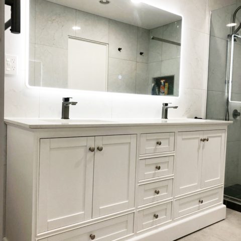 White bathroom vanity with illuminated mirror and modern faucets.