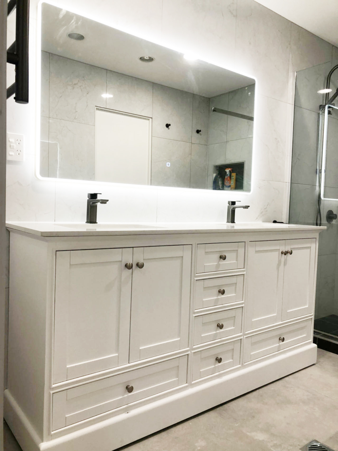 White bathroom vanity with illuminated mirror and modern faucets.