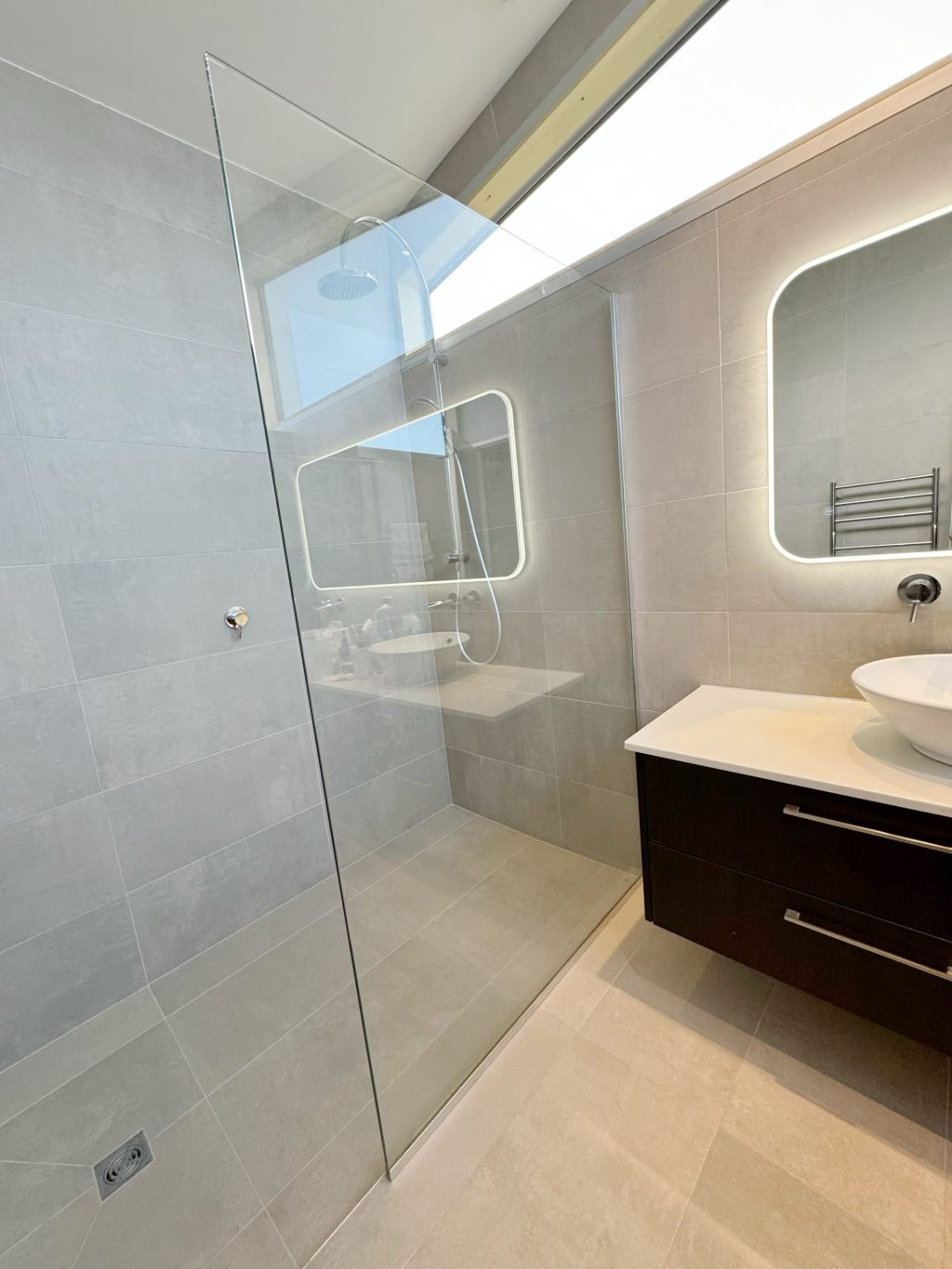 Modern bathroom with glass shower, illuminated mirror, and dark vanity with vessel sink.