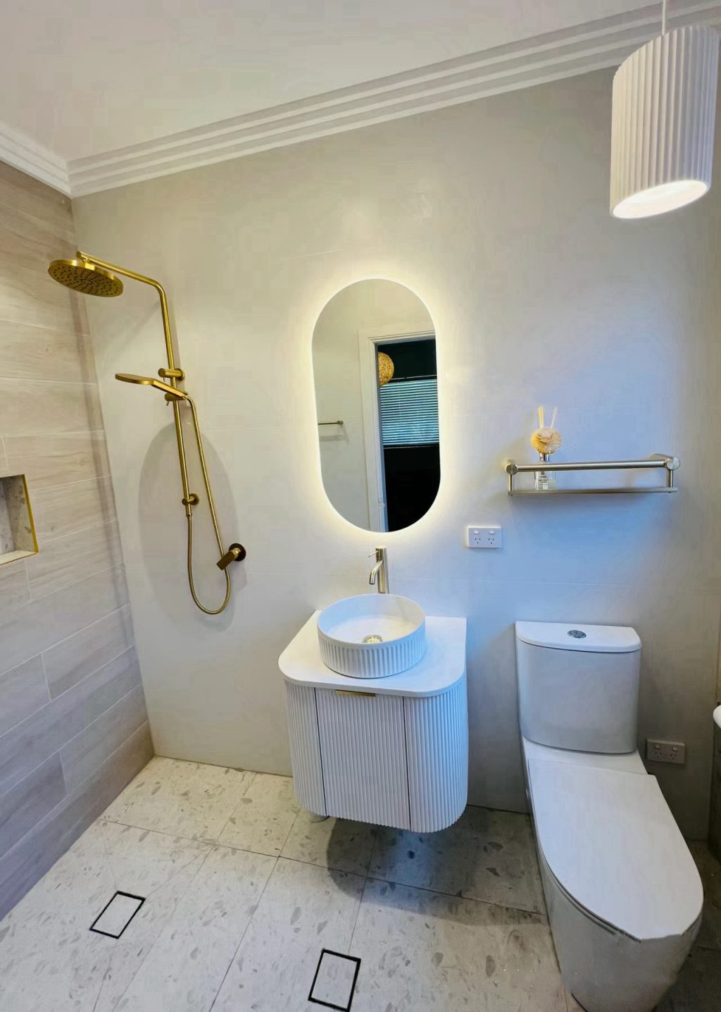 Modern bathroom with gold shower, oval mirror, and white fixtures.
