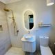 Modern bathroom with gold shower, oval mirror, and white fixtures.