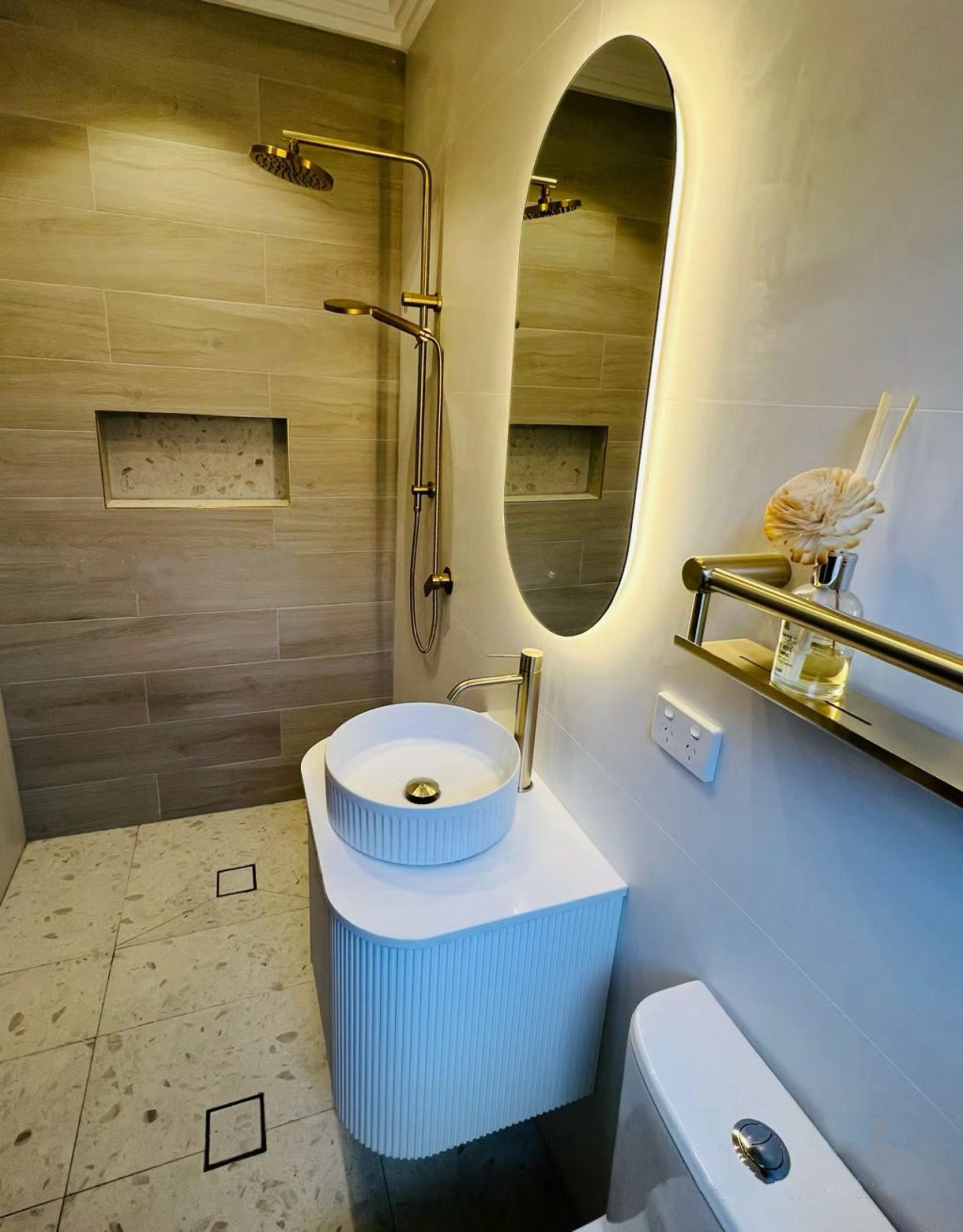 Modern bathroom with oval mirror, vessel sink, and gold fixtures.