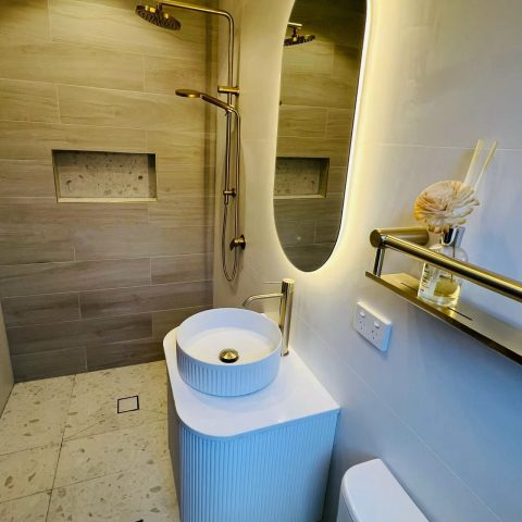 Modern bathroom with oval mirror, vessel sink, and gold fixtures.