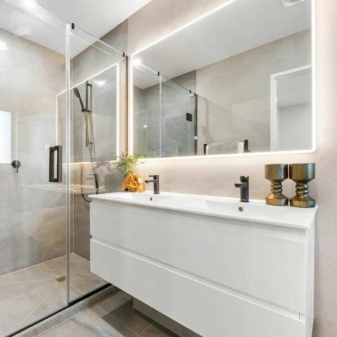 Modern bathroom with glass shower, illuminated mirror, and white vanity.