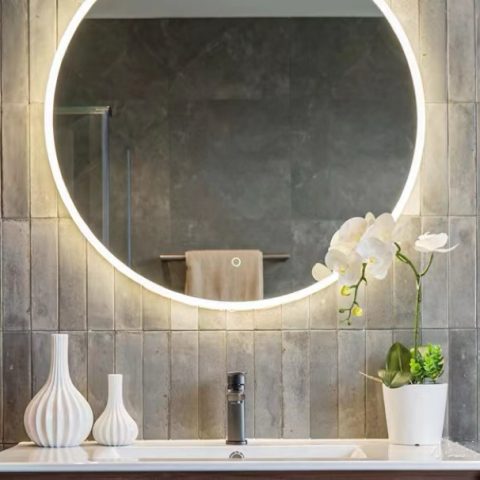 Modern bathroom with round mirror, white vases, and orchid plant.