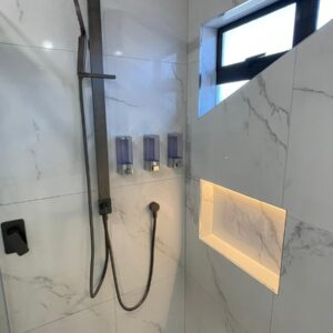 Modern shower with marble tiles, dual showerheads, and built-in shelf.