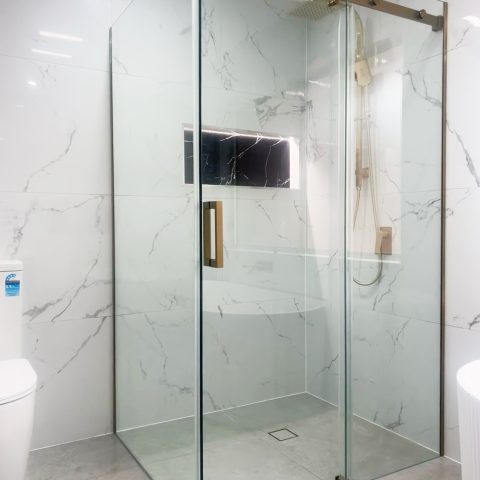 Modern bathroom with glass shower enclosure and marble walls.