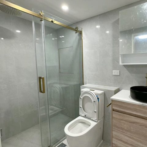 Modern bathroom with glass shower, toilet, and wooden vanity with black sink.