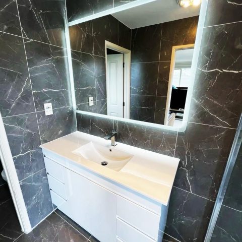 Modern bathroom with marble tiles and illuminated mirror above a white vanity.