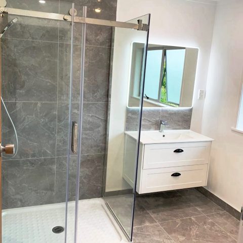 Modern bathroom with glass shower, gray tiles, and white vanity.