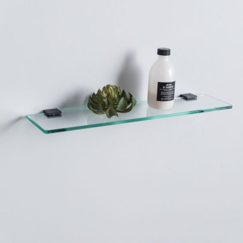 Glass shelf with a plant and a bottle against a white wall.