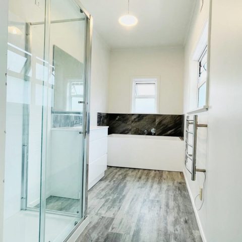 Modern bathroom with glass shower, white walls, and wood flooring.
