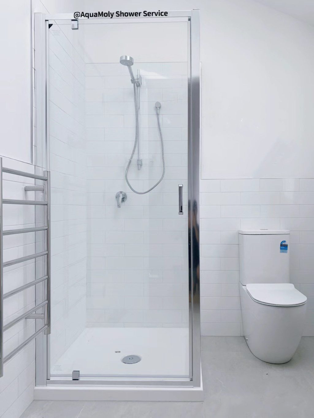 Modern bathroom with glass shower, white tiles, and toilet.