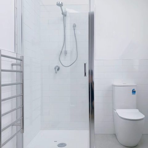 Modern bathroom with glass shower, white tiles, and toilet.