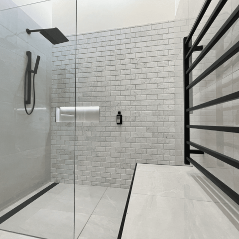 Modern shower with glass door, black fixtures, and white subway tiles.