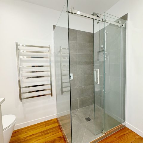 Modern bathroom with glass shower, gray tiles, and heated towel rack.