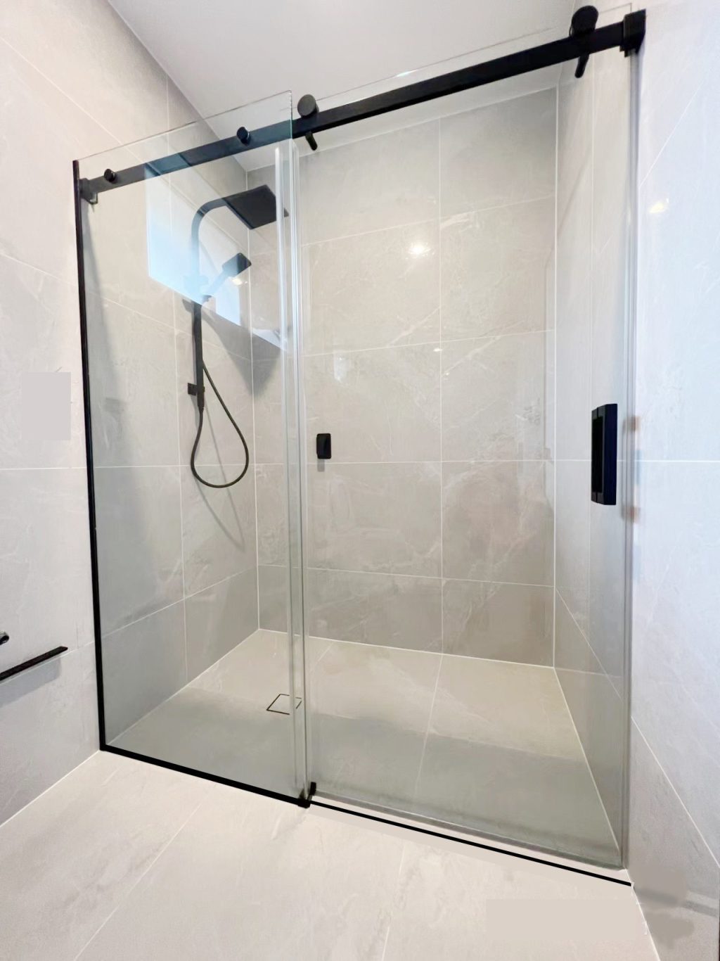 Glass shower enclosure with black fixtures in a modern bathroom.