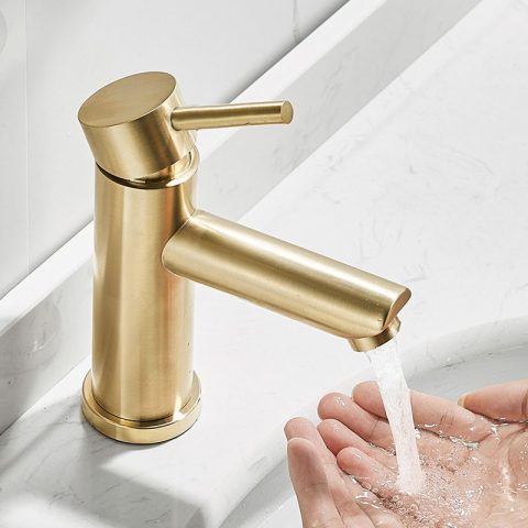 Gold faucet with running water over hands in a sink.