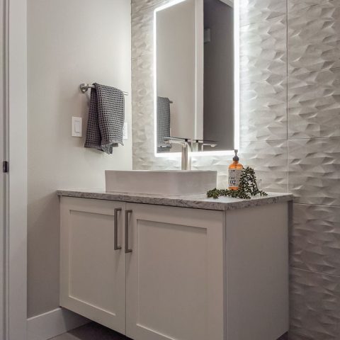 Modern bathroom vanity with illuminated mirror and textured wall.