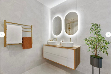 Modern bathroom with double sinks, oval mirrors, and a towel rack.