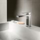 Modern chrome faucet on white bathroom sink with soap and cups.